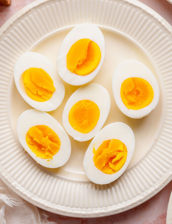 Fully cooked hard boiled eggs cut in half on a white plate, showing firm, bright yellow yolks and smooth whites.