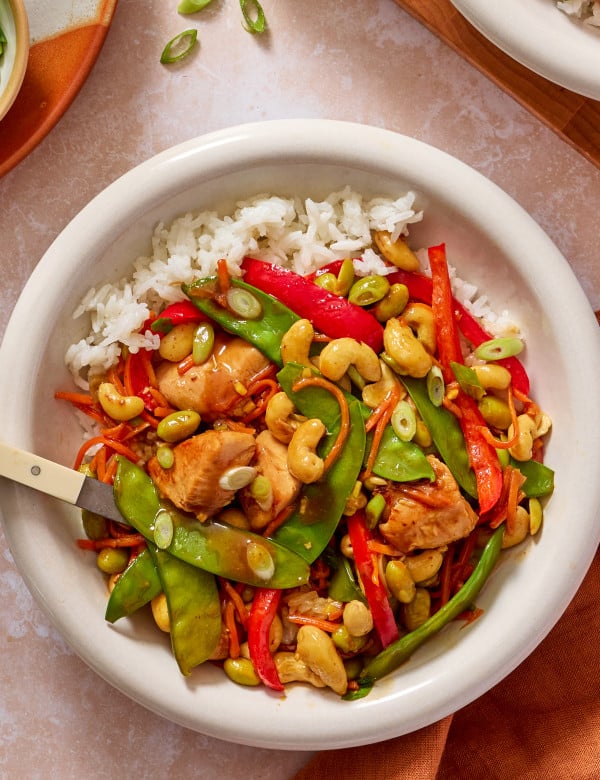Cashew chicken in a bowl with rice, green onions and a fork on the side.