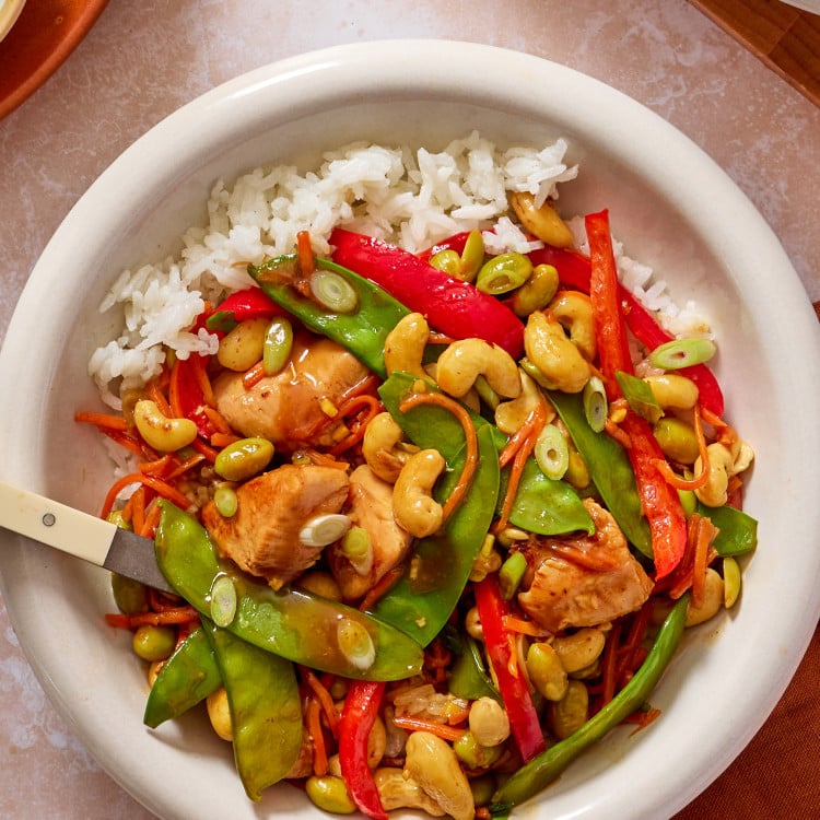Cashew chicken in a bowl with rice, green onions and a fork on the side.
