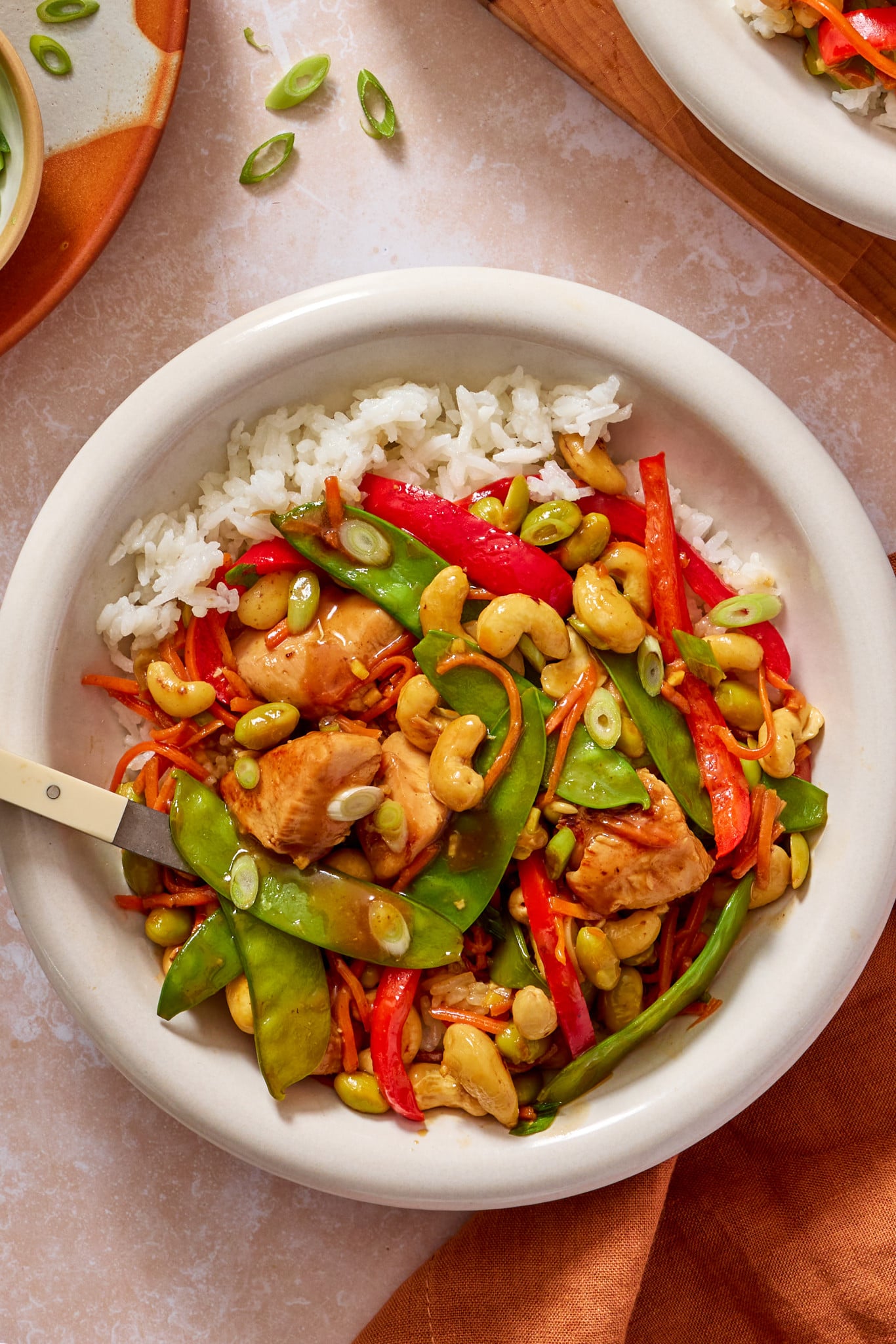 Cashew chicken in a bowl with rice, green onions and a fork on the side.