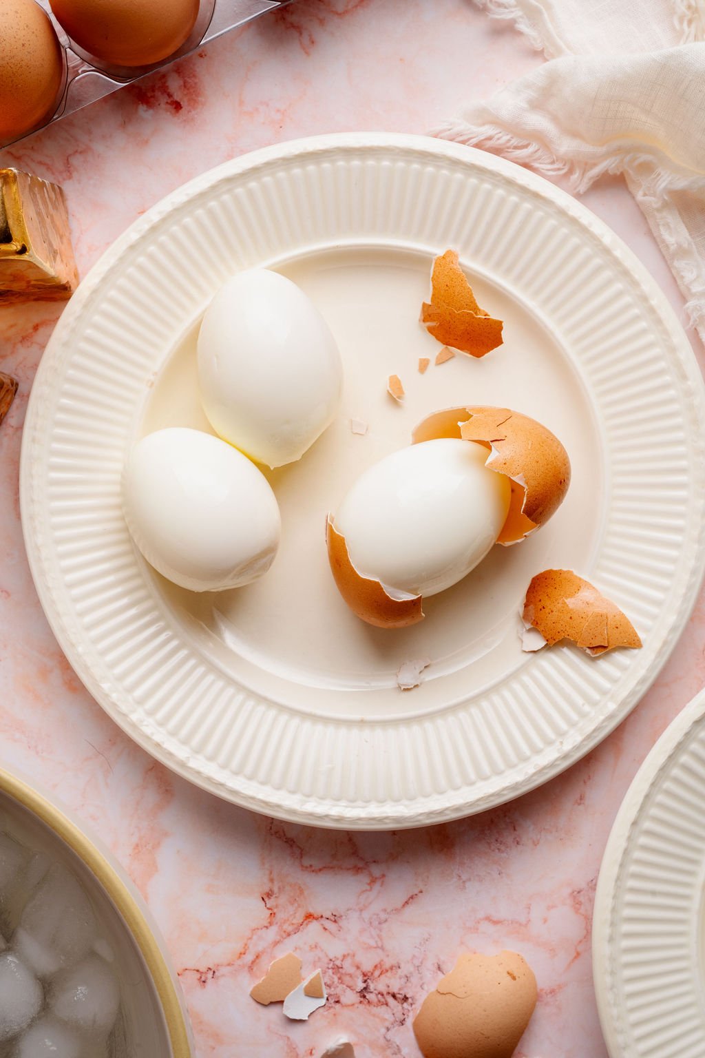 Three peeled hard boiled eggs on a white plate with broken eggshells, showing how cleanly the shells release.
