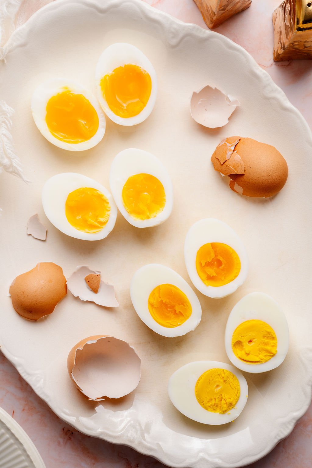 Hard boiled eggs cut in half on a white platter, displaying different yolk doneness from jammy and custardy to fully set.