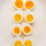 Overhead view of hard boiled eggs cut in half and arranged on a white platter, showing different yolk doneness from jammy and custardy to fully set and firm.