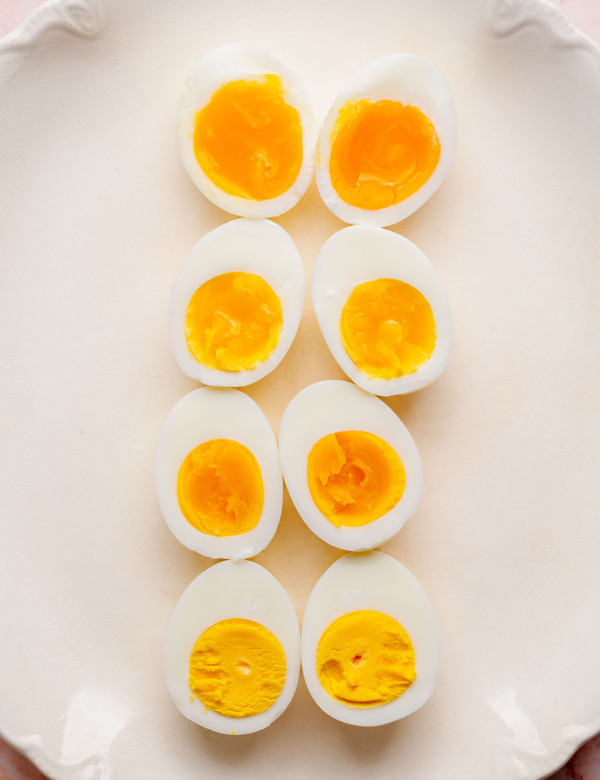 Overhead view of hard boiled eggs cut in half and arranged on a white platter, showing different yolk doneness from jammy and custardy to fully set and firm.