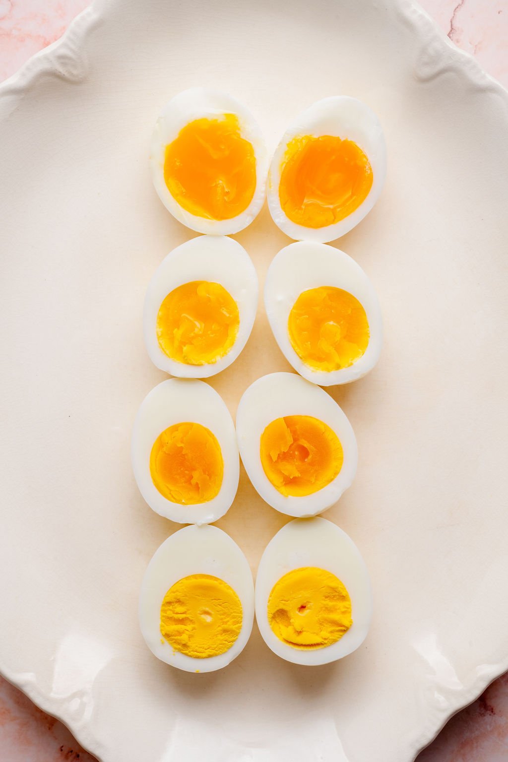 Overhead view of hard boiled eggs cut in half and arranged on a white platter, showing different yolk doneness from jammy and custardy to fully set and firm.