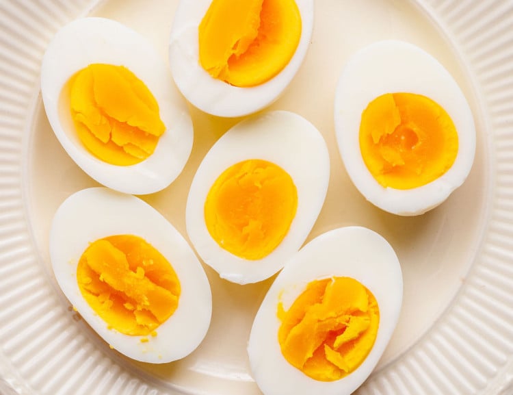 Fully cooked hard boiled eggs cut in half on a white plate, showing firm, bright yellow yolks and smooth whites.