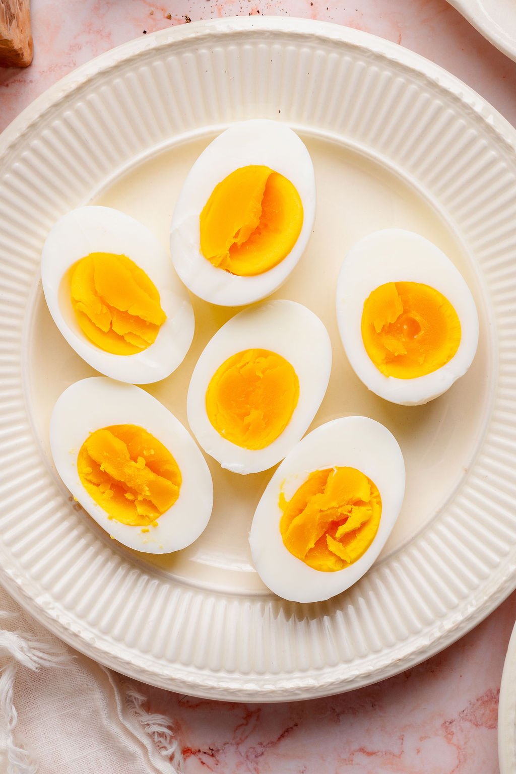 Fully cooked hard boiled eggs cut in half on a white plate, showing firm, bright yellow yolks and smooth whites.