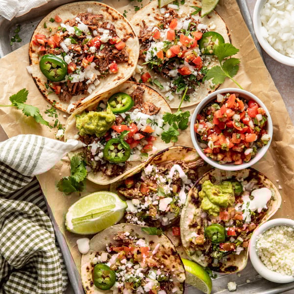 Beef barbacoa tacos assembled on large baking sheet.