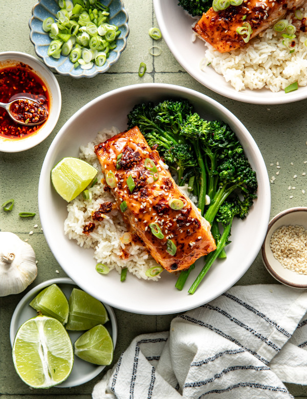 Chili crisp salmon plated in a bowl with broccolini, rice and a wedge of lime.