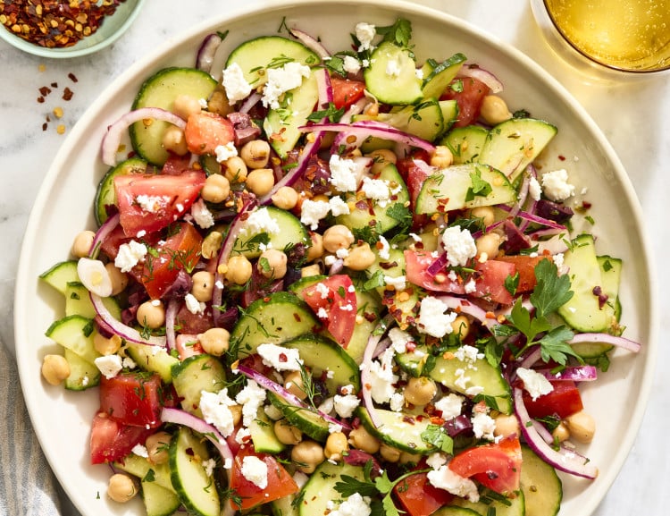 Cucumber tomato salad tossed and served on large serving plate.
