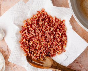 Cooked bacon transferred to a paper-towel-lined plate to drain excess grease while cooking the onions.