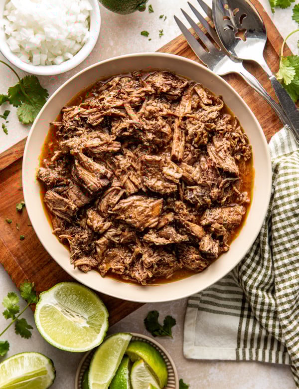 Shredded beef barbacoa in a bowl on top of a wooden serving tray.