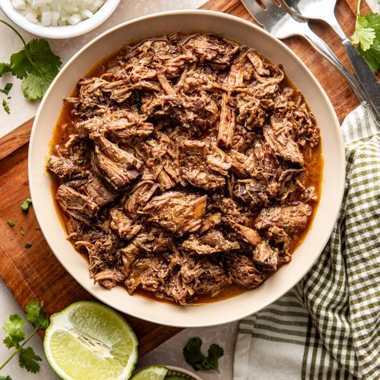 Shredded beef barbacoa in a bowl on top of a wooden serving tray.