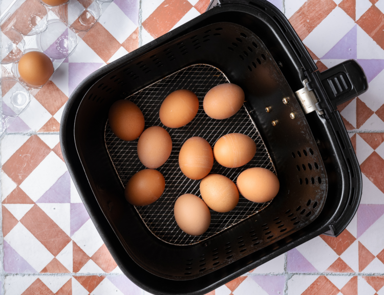 Ten brown eggs placed in a single layer in the air fryer basket.