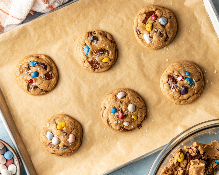 Six cadbury cookies baked on parchment-lined baking sheet and garnished with flaky salt after baking.