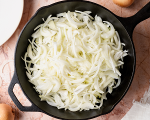 Adding the sliced yellow onions to a cast-iron pan.