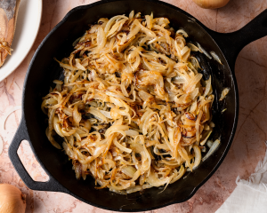 Onions starting to cook down in a cast-iron pan halfway through cooking them to caramelized.