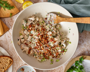 Adding chopped pecans to chicken salad in mixing bowl.