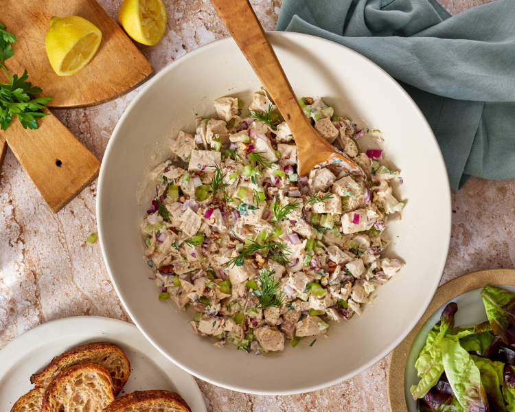 Chicken salad mixed together in large mixing bowl with wood spoon.