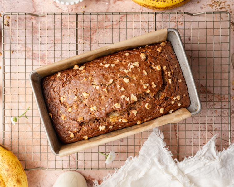 Healthy banana bread baked in an light-colored aluminum pan lined with parchment paper.