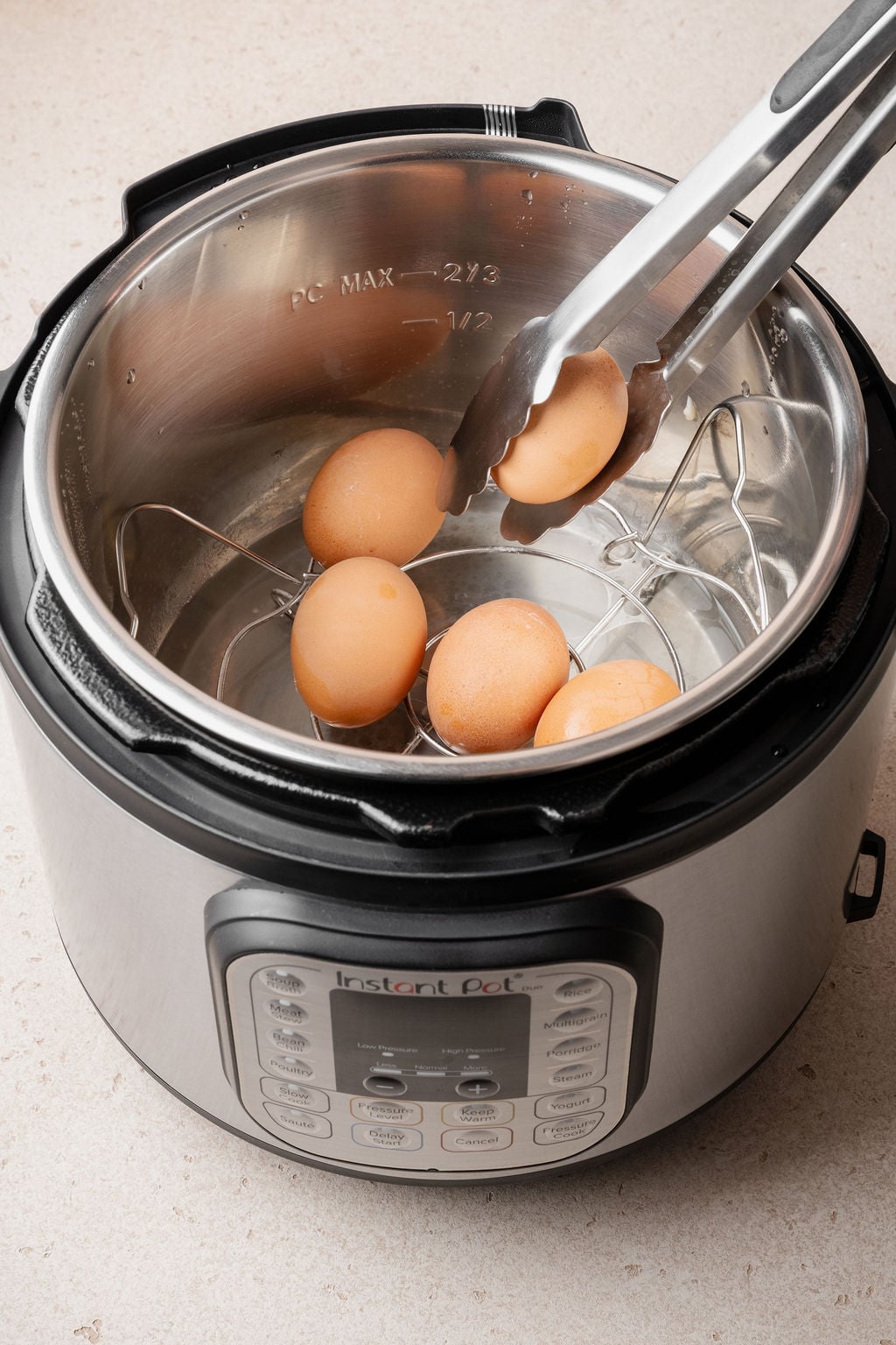 Using tongs to place eggs onto the trivet inside an Instant Pot insert to cook hard boiled eggs.