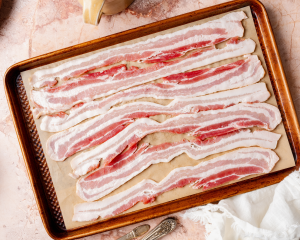 Seven pieces of bacon arranged on a prepared baking sheet.