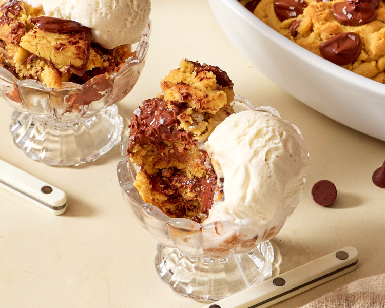Bite taken out of scoopable cookie in glass bowl with a scoop of vanilla ice cream on the side.