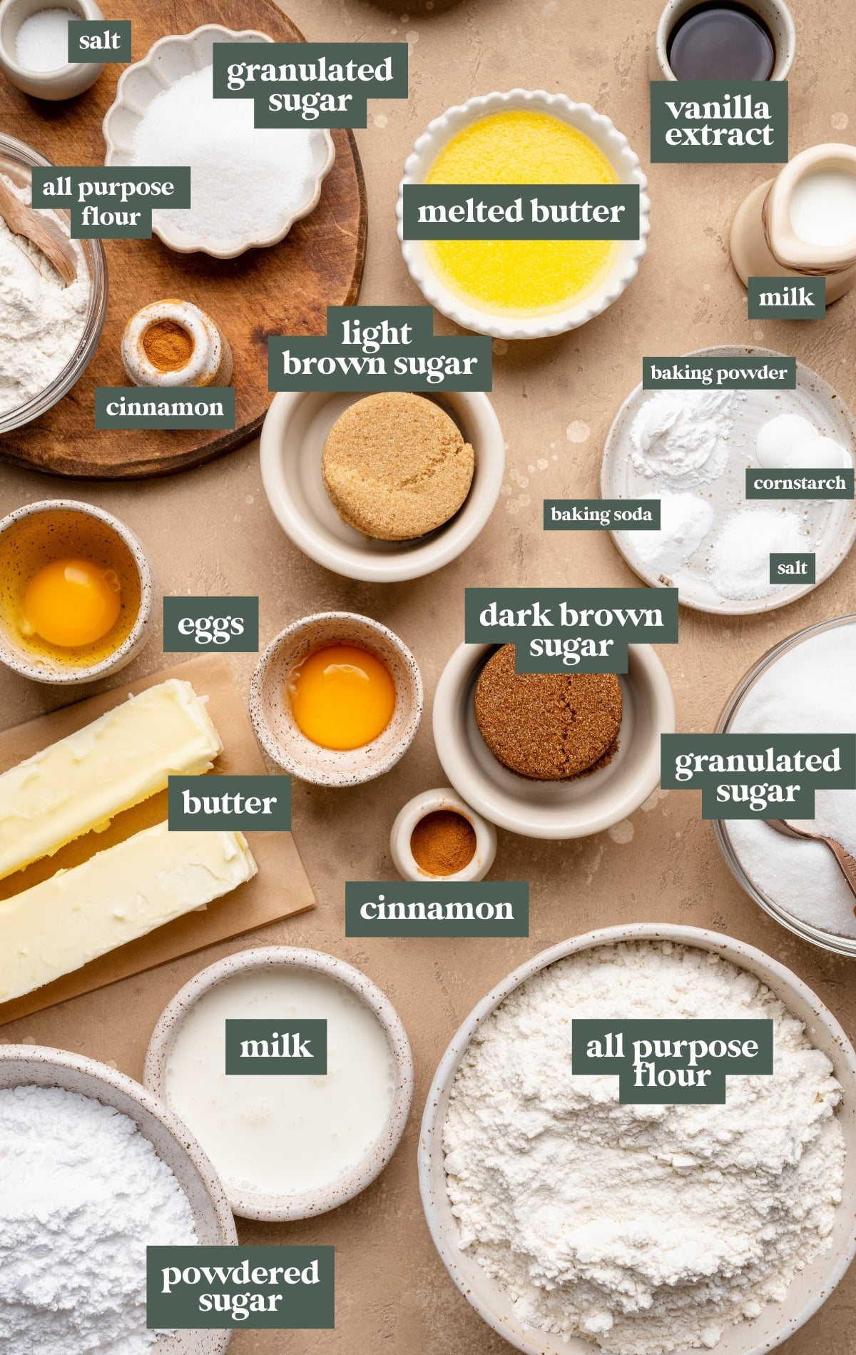 Overhead collage of baking ingredients for coffee cake cookies including all-purpose flour, granulated sugar, light and dark brown sugar, powdered sugar, melted butter, butter sticks, eggs, milk, vanilla extract, cinnamon, baking powder, baking soda, cornstarch, and salt arranged in small bowls on a neutral countertop.