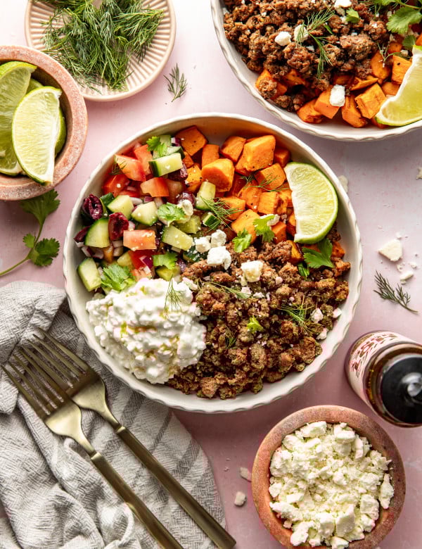 Mediterranean ground beef sweet potato bowls served in large bowl and garnished with fresh herbs and lime wedge.
