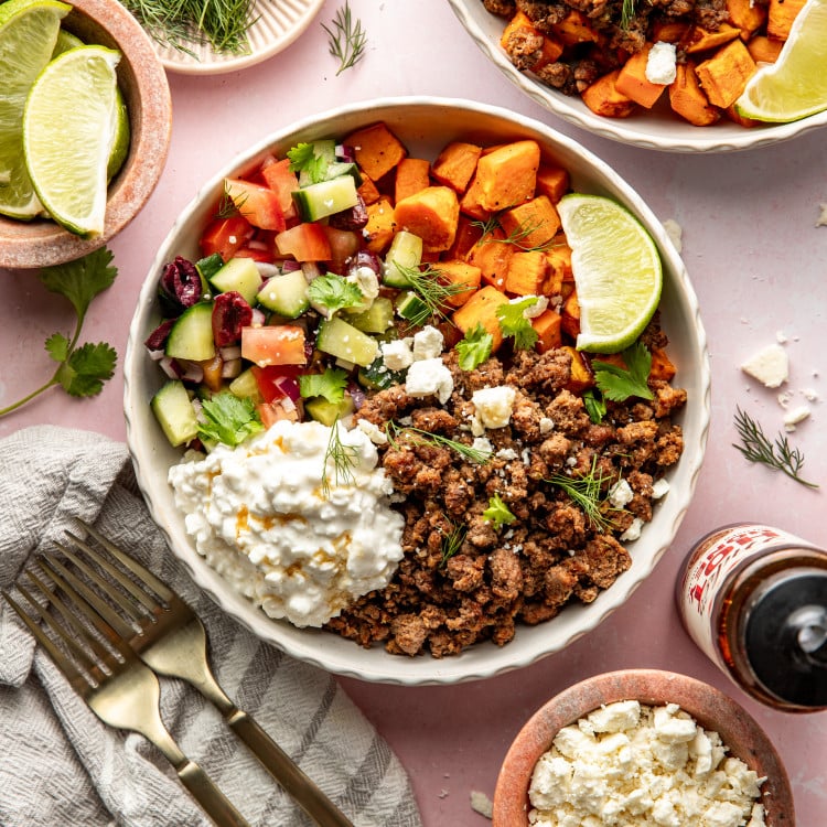 Mediterranean ground beef sweet potato bowls served in large bowl and garnished with fresh herbs and lime wedge.