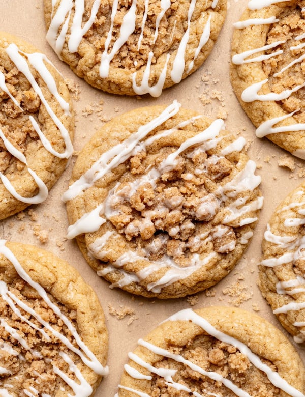 Overhead view of multiple coffee cake cookies arranged on parchment paper, each topped with crumb streusel and finished with a light white glaze drizzle.