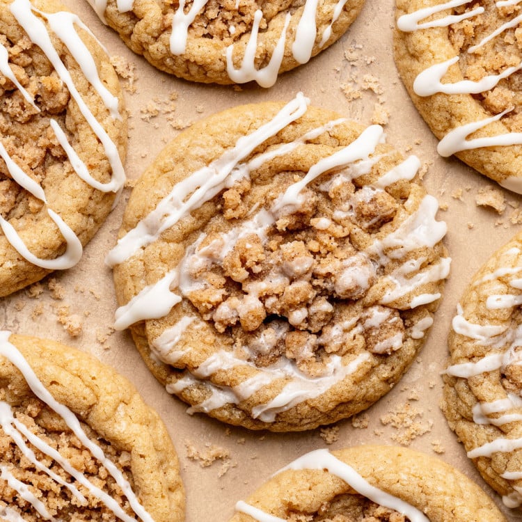 Overhead view of multiple coffee cake cookies arranged on parchment paper, each topped with crumb streusel and finished with a light white glaze drizzle.