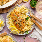 Chicken piccata served on top of spaghetti pasta on a plate with fork and knife.