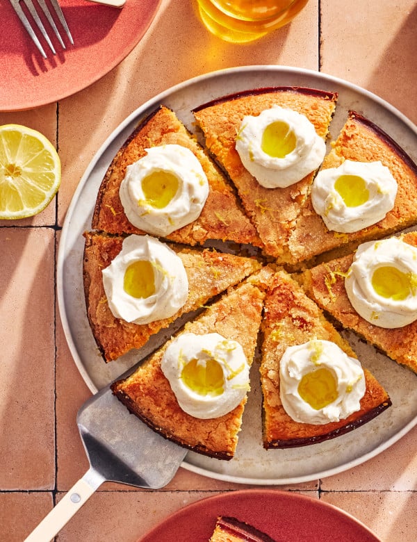 Lemon olive oil ricotta cake sliced and topped with dollops of whipped ricotta topping, olive oil and lemon zest.