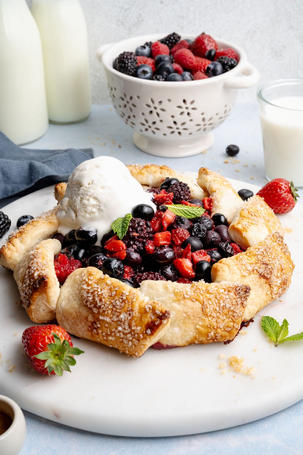 Close-up angled view of a baked mixed berry galette with a scoop of melting vanilla ice cream, highlighting the golden, flaky crust and vibrant berry filling.