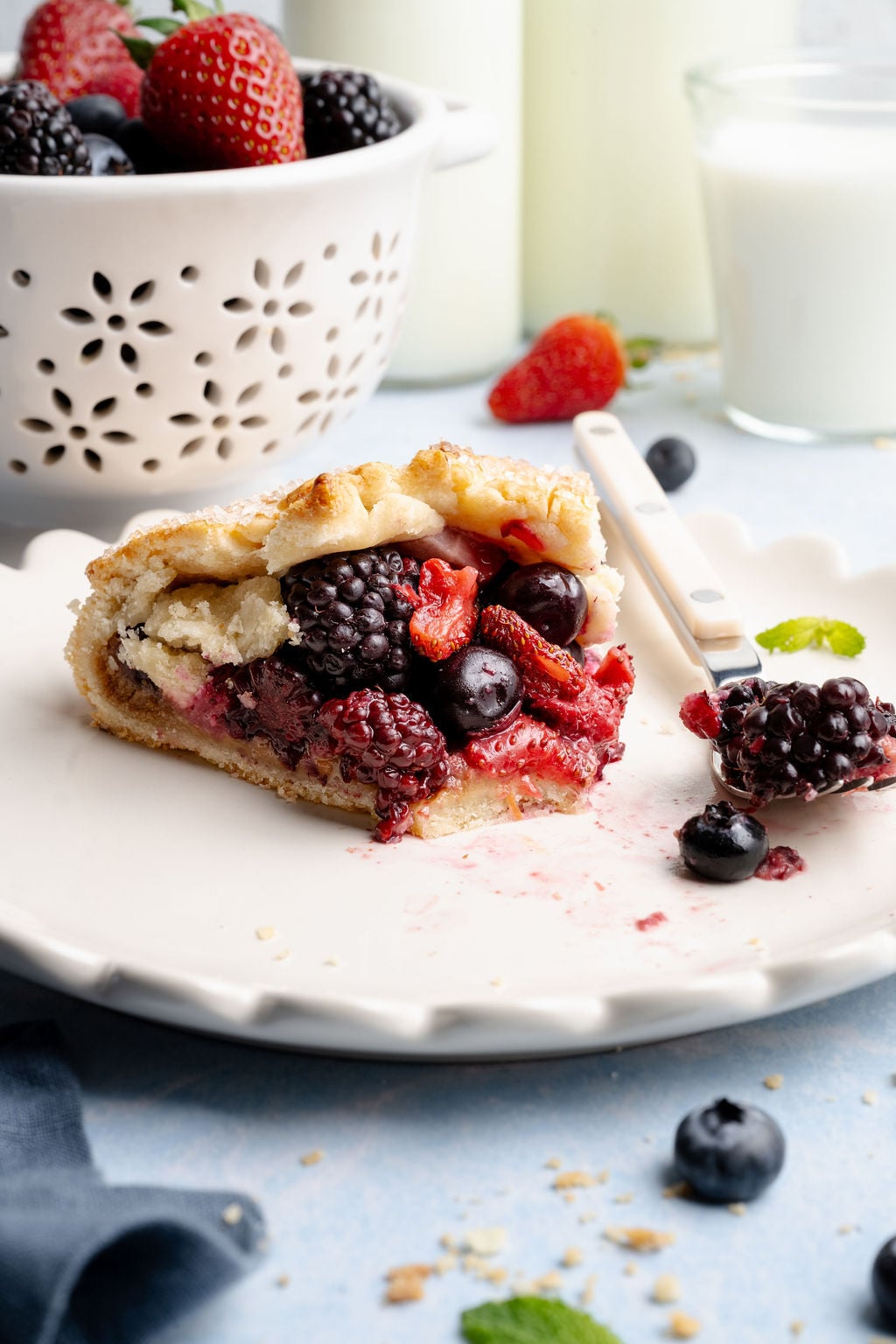 Close-up of a slice of mixed berry galette on a plate with a fork, showing the juicy berry filling and tender, buttery crust with crumbs scattered around.
