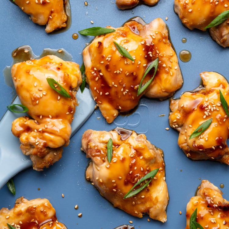 Oven baked teriyaki chicken thighs on a baking tray garnished with green onions and sesame seeds.