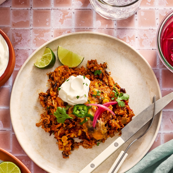 Chicken and rice enchilada casserole on a plate garnished with pickled red onions, jalapenos, sour cream and cilantro.