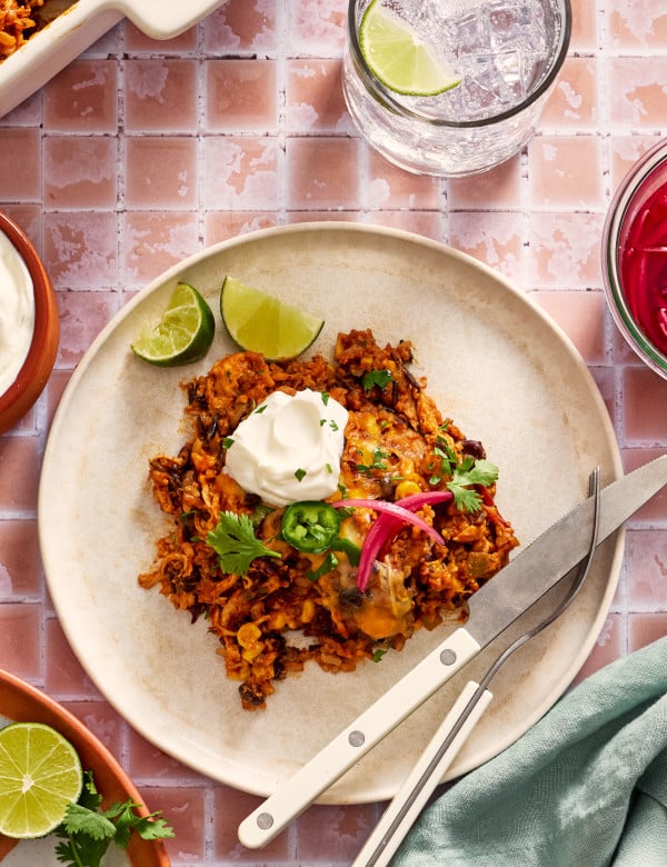 Chicken and rice enchilada casserole on a plate garnished with pickled red onions, jalapenos, sour cream and cilantro.