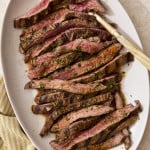 Sliced grilled carne asada on a plate with gold serving fork on the right side.