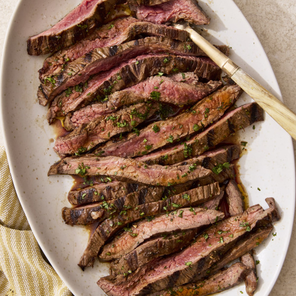 Sliced grilled carne asada on a plate with gold serving fork on the right side.