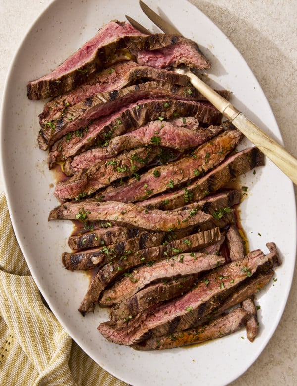 Sliced grilled carne asada on a plate with gold serving fork on the right side.