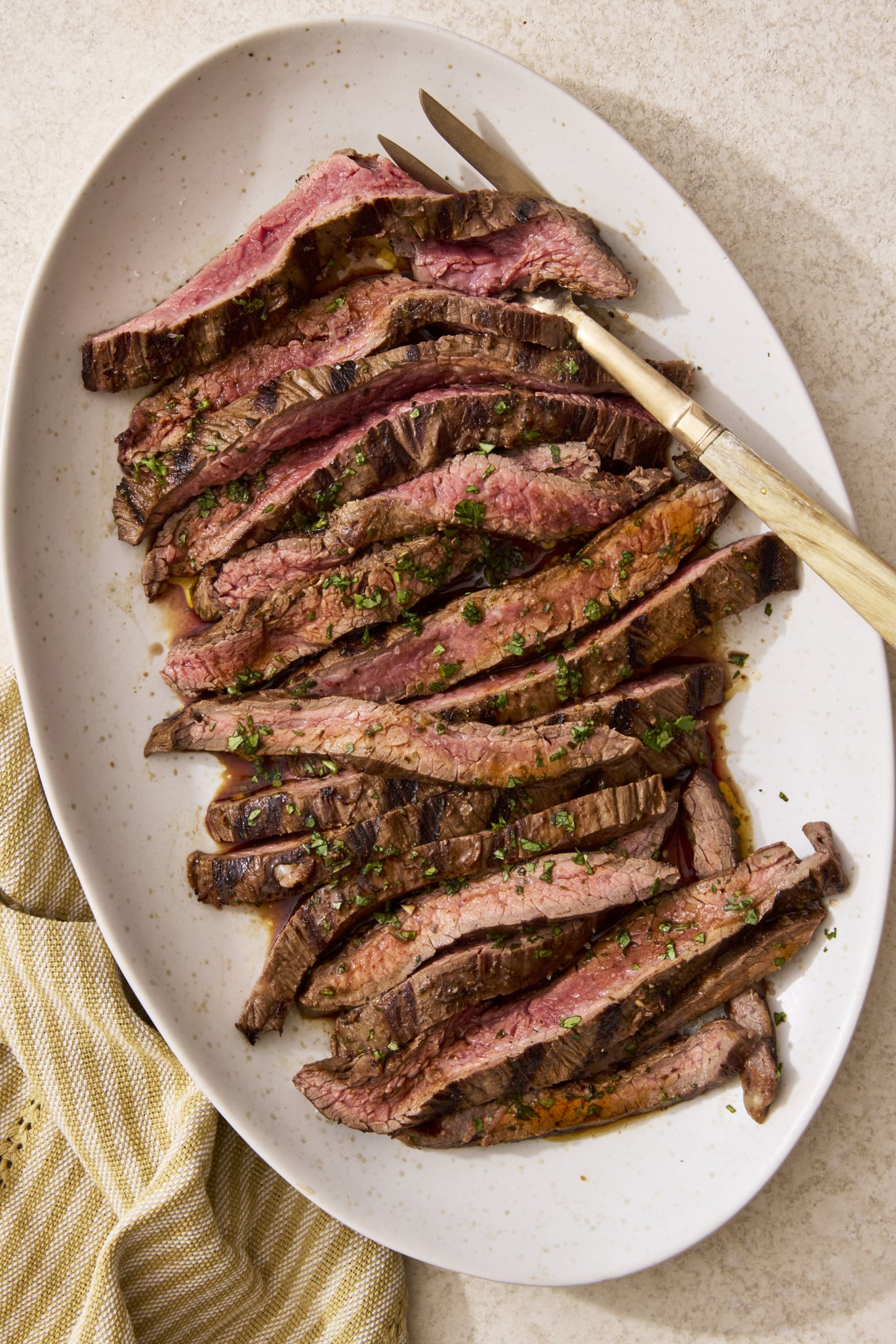 Sliced grilled carne asada on a plate with gold serving fork on the right side.