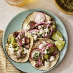 Three carne asada tacos on a blue plate with toppings.
