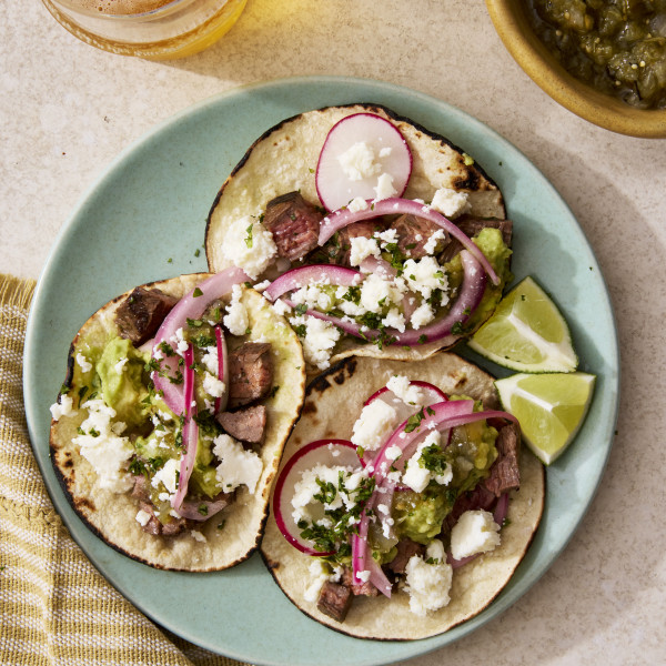 Three carne asada tacos on a blue plate with toppings.
