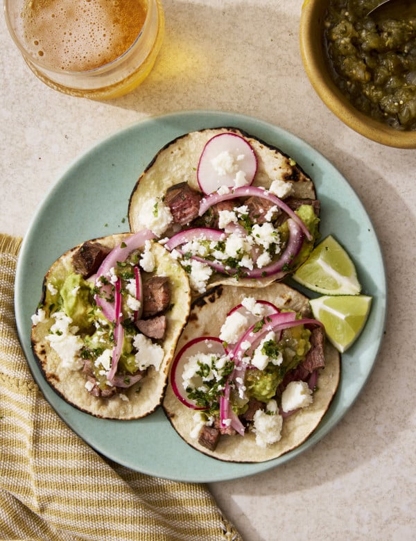 Three carne asada tacos on a blue plate with toppings.