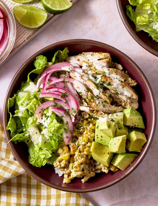 Street corn chicken bowl topped with avocado, lettuce and pickled onions.