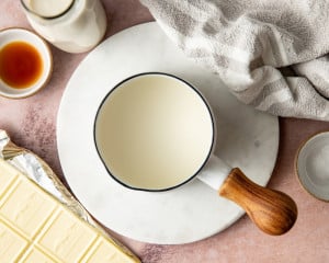Overhead step-by-step collage demonstrating how to bloom gelatin by sprinkling gelatin over water, allowing it to hydrate, stirring the gelatin mixture, pouring the dissolved gelatin into melted white chocolate, and stirring until fully incorporated.