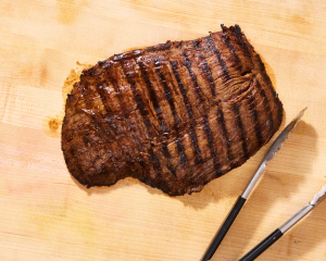 Letting the grilled carne asada rest on a cutting board before slicing.