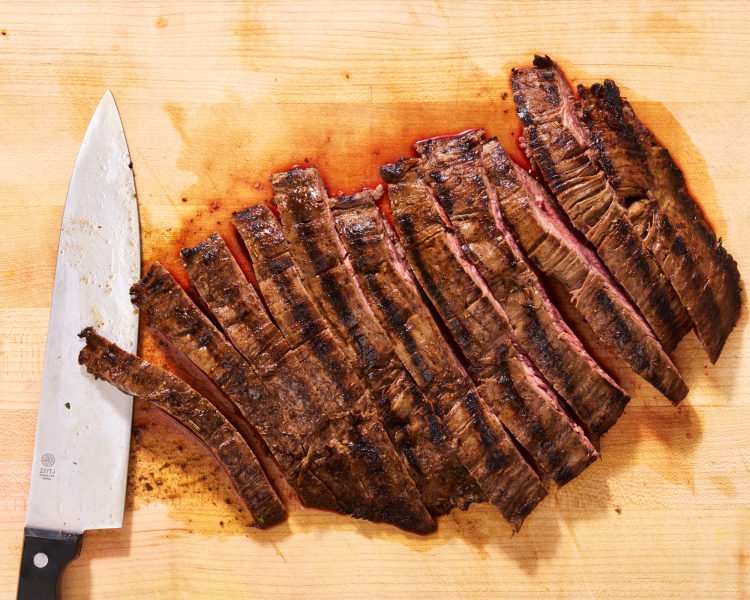 Slicing the cooked flank streak against the grain on a cutting board.